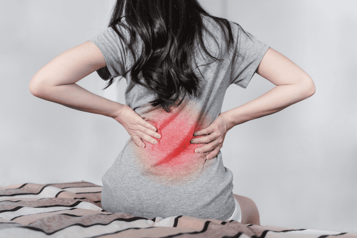 Person seen from behind, holding lower back with a red glow indicating back pain.